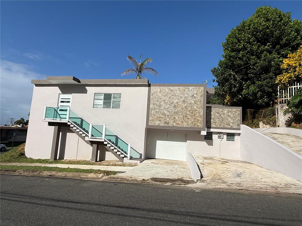 A two-story house with a stone-accented facade, a garage, and an external glass-railed staircase — 21 Andes MONTEREY, SAN JUAN, PR