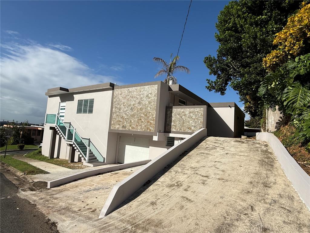 A two-story house features a concrete driveway, stone facade accents, and an exterior staircase — 21 Andes MONTEREY, SAN JUAN, PR
