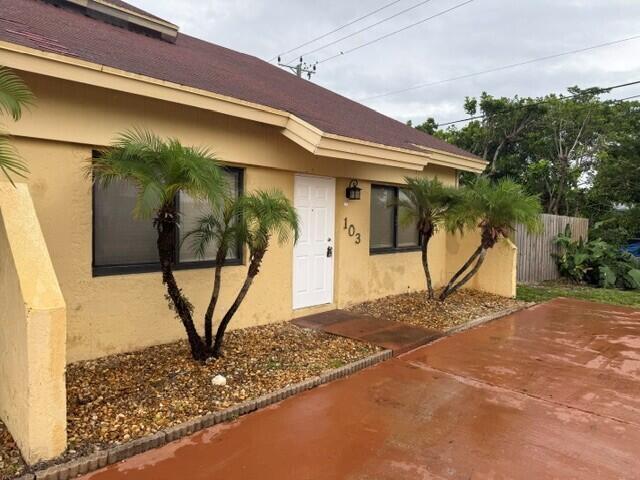The exterior of a yellow, single-story house features a white front door and palm trees — 103 NE 28th Street, Boca Raton FL 33431, BOCA RATON, FL