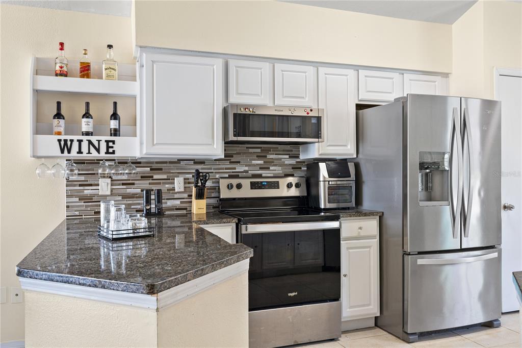 A kitchen features white cabinets, stainless steel appliances, a granite countertop, and a wine rack — 2629 CHATHAM CIRCLE, KISSIMMEE, FL