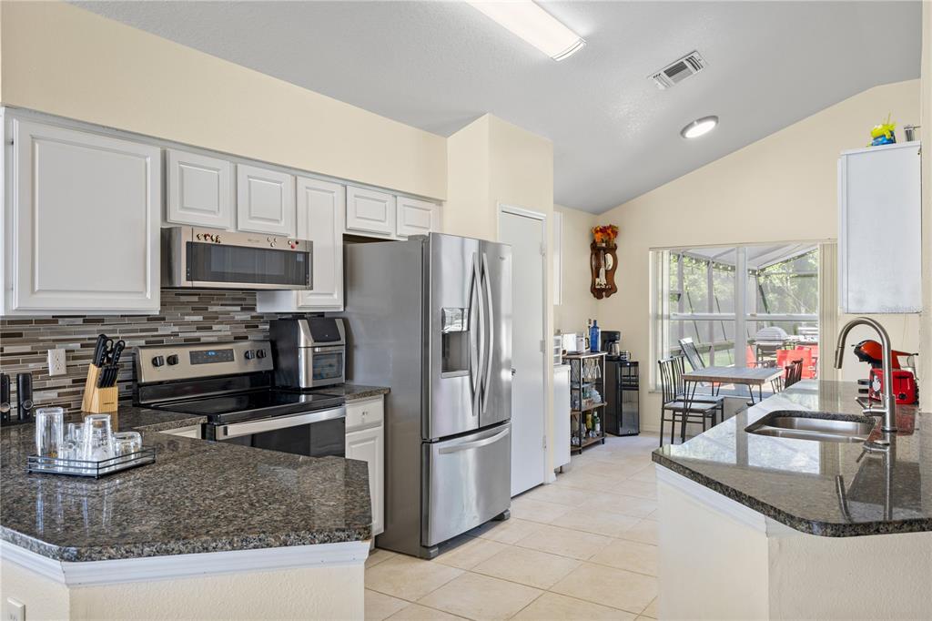 A kitchen features white cabinets, granite countertops, stainless steel appliances, and a tiled floor — 2629 CHATHAM CIRCLE, KISSIMMEE, FL