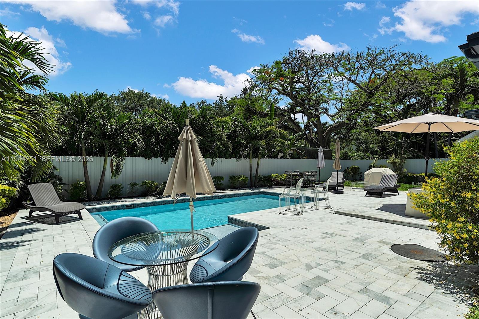 A backyard patio features a swimming pool, lounge chairs, and a dining set under umbrellas — 660 NE 121st St, Biscayne Park FL 33161, BISCAYNE PARK, FL