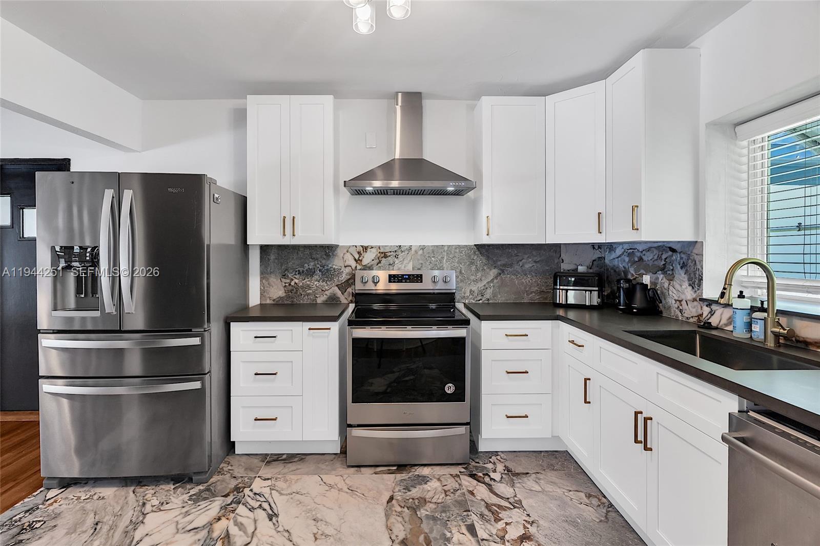 A kitchen features white cabinets, stainless steel appliances, dark countertops, and a marble backsplash — 660 NE 121st St, Biscayne Park FL 33161, BISCAYNE PARK, FL