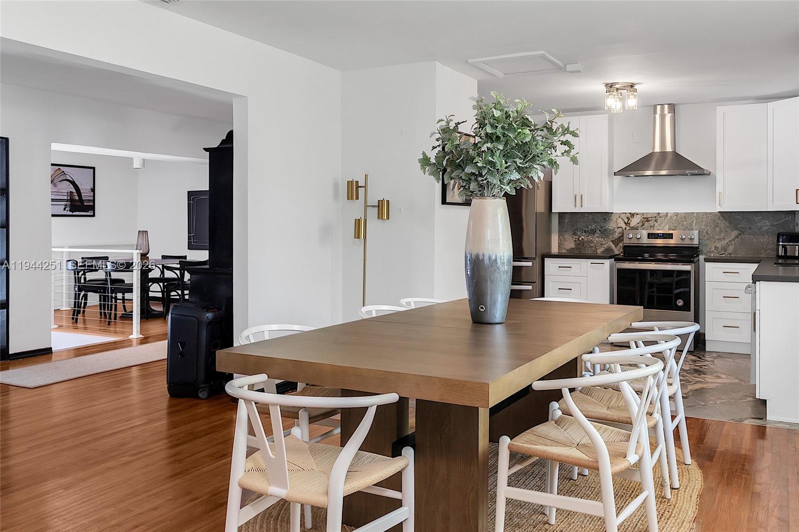 A dining area with a wooden table and white chairs sits adjacent to a modern kitchen — 660 NE 121st St, Biscayne Park FL 33161, BISCAYNE PARK, FL