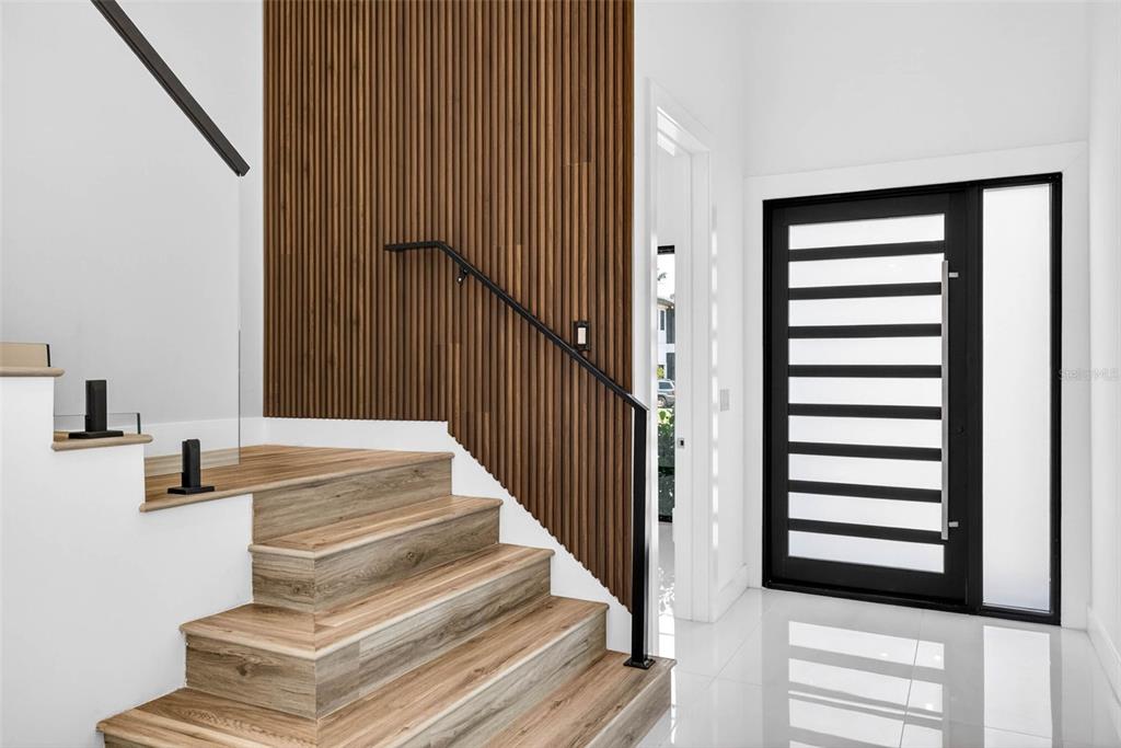 A modern entryway features wood-slat wall paneling, a floating staircase, and a black-framed glass door — 4426 W EUCLID AVENUE, TAMPA, FL