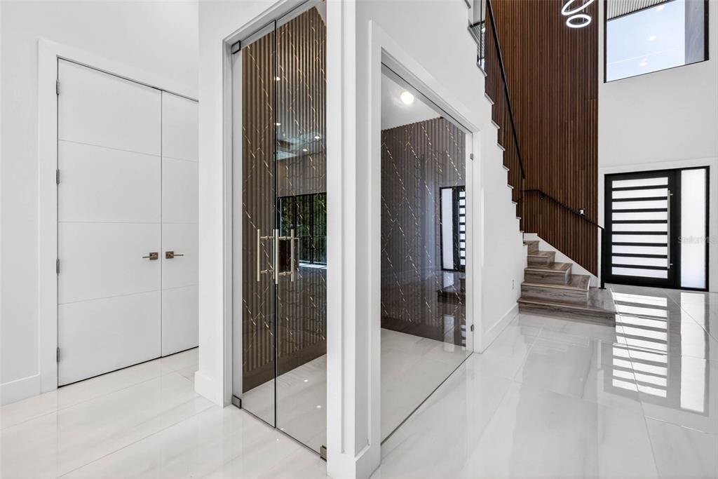 A modern foyer features a glass-enclosed wine room, white tile floors, and a wood-paneled staircase — 4426 W EUCLID AVENUE, TAMPA, FL