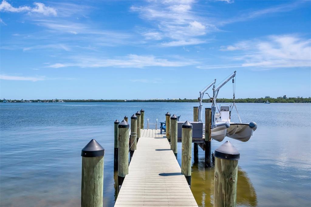 A wooden boat dock extends into calm water with a boat lift and small vessel — 3863 CATALINA DRIVE, BRADENTON, FL
