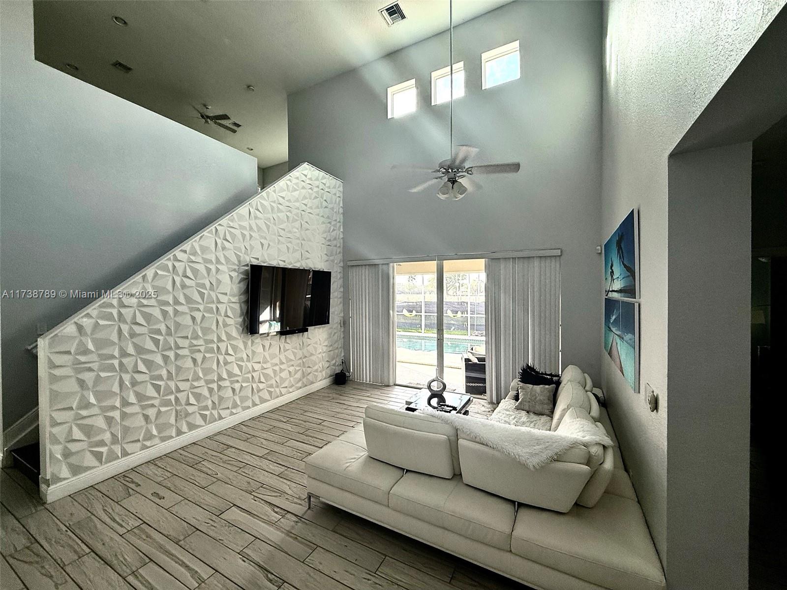 A living room with a white sectional sofa, high ceilings, and a view of a pool — 2602 Augusta Dr, Homestead FL 33035, HOMESTEAD, FL