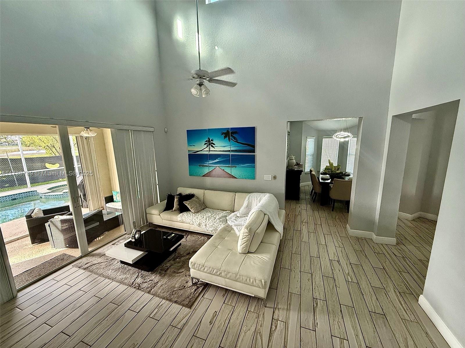 A living room features a dark staircase, high ceilings, and sliding glass doors to a patio — 2602 Augusta Dr, Homestead FL 33035, HOMESTEAD, FL