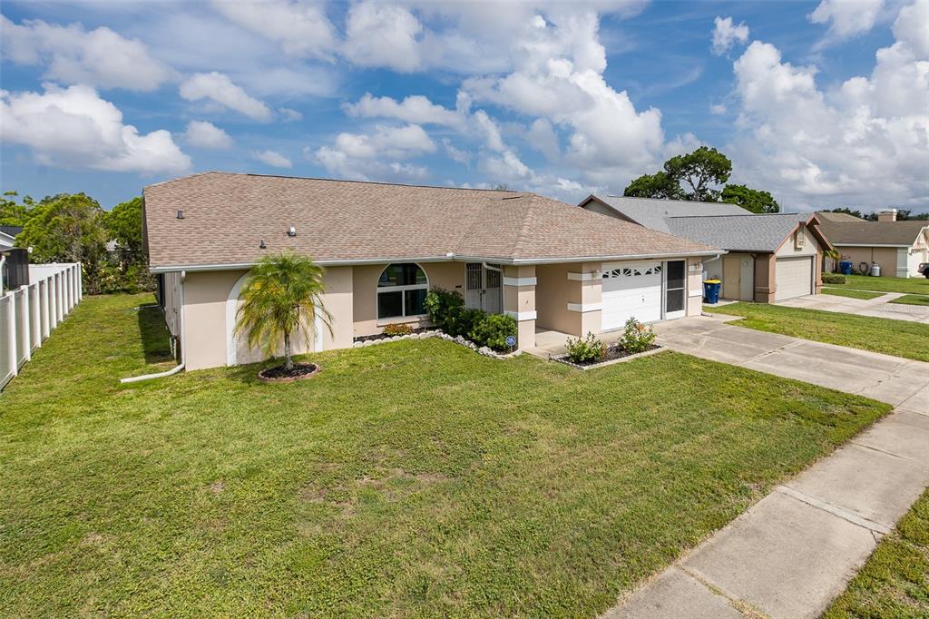A single-story house with a tan stucco exterior, a shingled roof, and a front lawn — 4515 COUNTY BREEZE DRIVE, NEW PORT RICHEY, FL