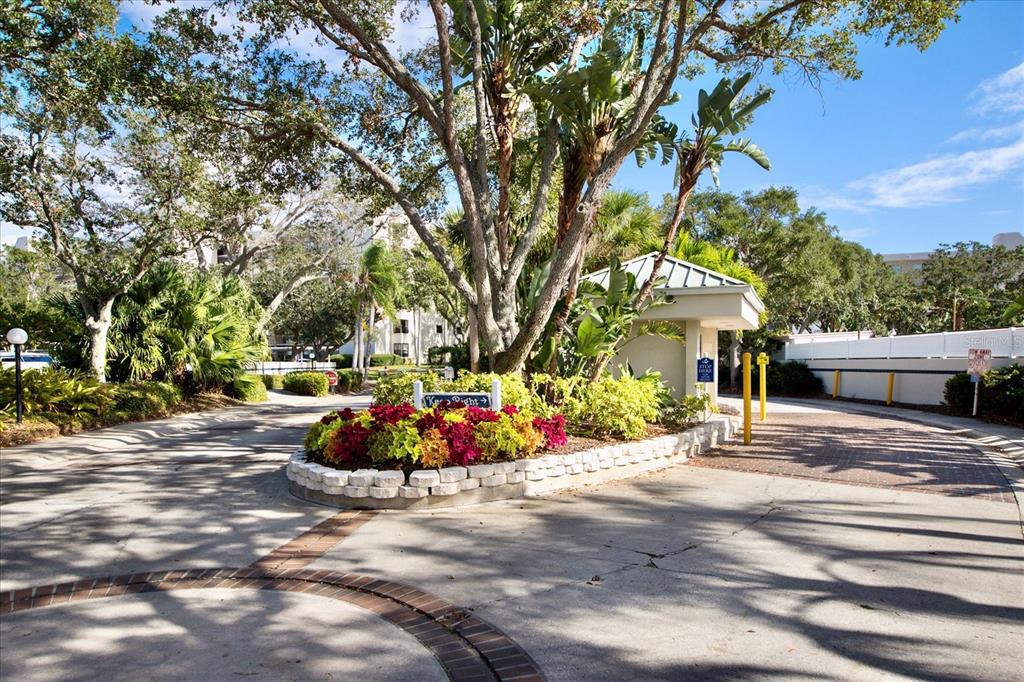 A gated entrance with a brick-lined driveway, lush landscaping, and a small guardhouse — 1324 PASADENA AVENUE S UNIT 204, SOUTH PASADENA, FL