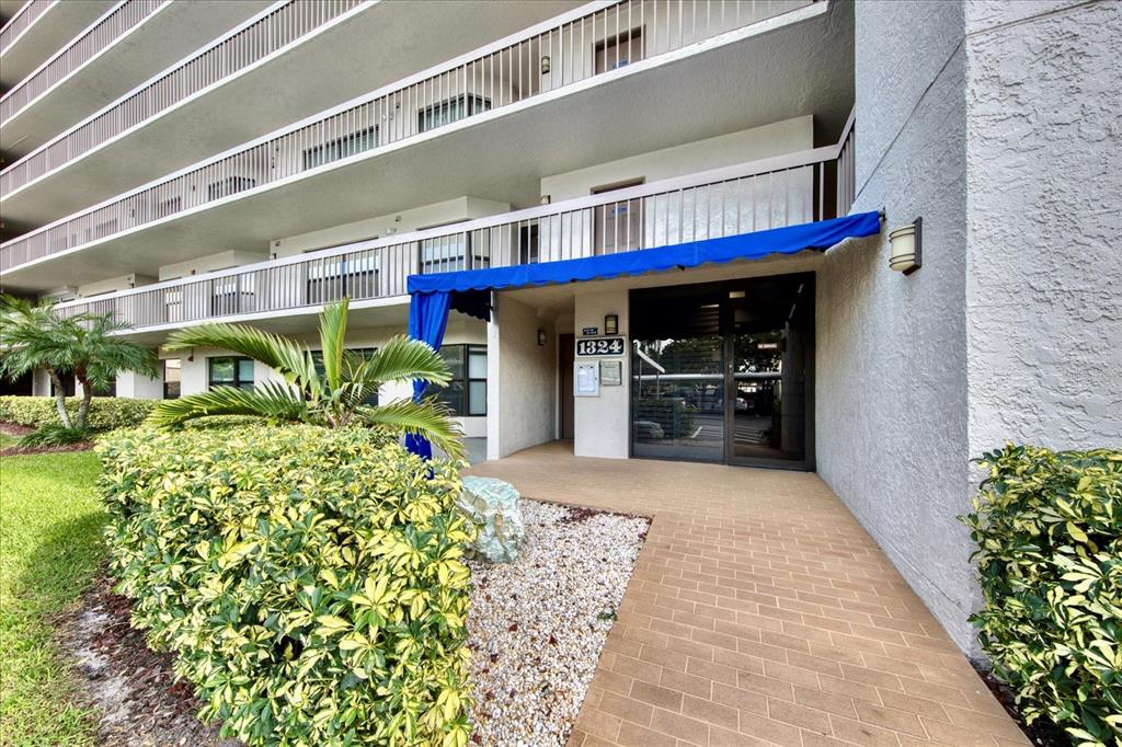 The exterior entrance of a multi-story apartment building features a blue awning and walkway — 1324 PASADENA AVENUE S UNIT 204, SOUTH PASADENA, FL
