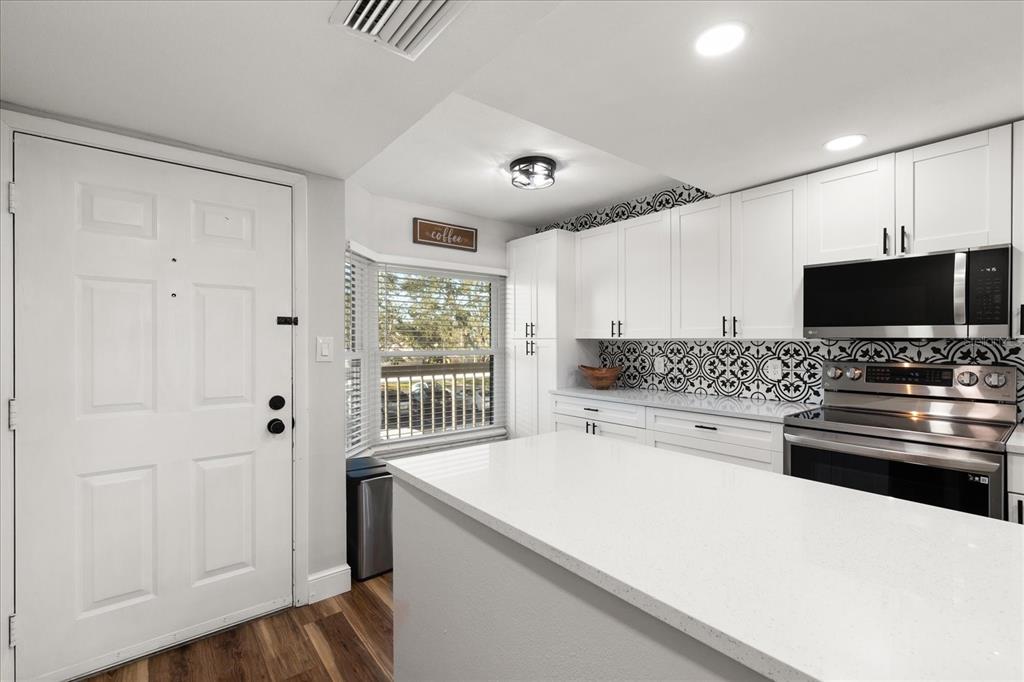 A kitchen features white cabinets, a quartz island, and a patterned tile backsplash — 1324 PASADENA AVENUE S UNIT 204, SOUTH PASADENA, FL
