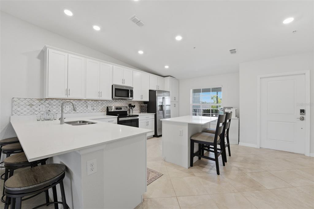A modern kitchen features white cabinetry, a quartz island with seating, and light tile flooring — 12440 WELLEN GOLF STREET UNIT 201, VENICE, FL