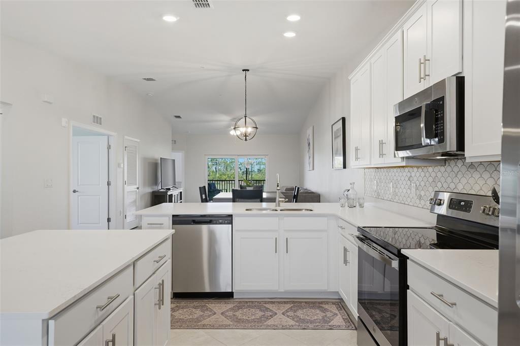 A white kitchen with stainless steel appliances, quartz countertops, and a view of the dining area — 12440 WELLEN GOLF STREET UNIT 201, VENICE, FL