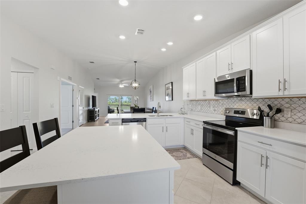 A modern kitchen features white cabinets, stainless steel appliances, and a large quartz-topped island — 12440 WELLEN GOLF STREET UNIT 201, VENICE, FL