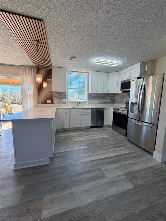 A modern kitchen features white cabinetry, stainless steel appliances, and a wood-slat ceiling accent — 2689 COURTLAND BOULEVARD, DELTONA, FL