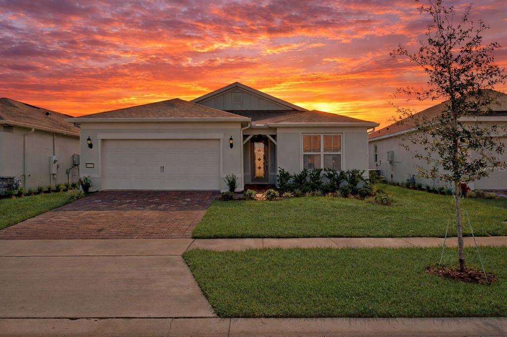 A single-story suburban house with a brick driveway and a sunset sky in the background — 6354 SHIMMERING SHORES LANE, ST CLOUD, FL