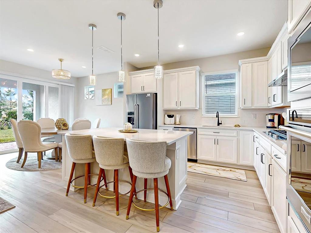 A modern kitchen features white cabinetry, a central island with bar stools, and light flooring — 6354 SHIMMERING SHORES LANE, ST CLOUD, FL