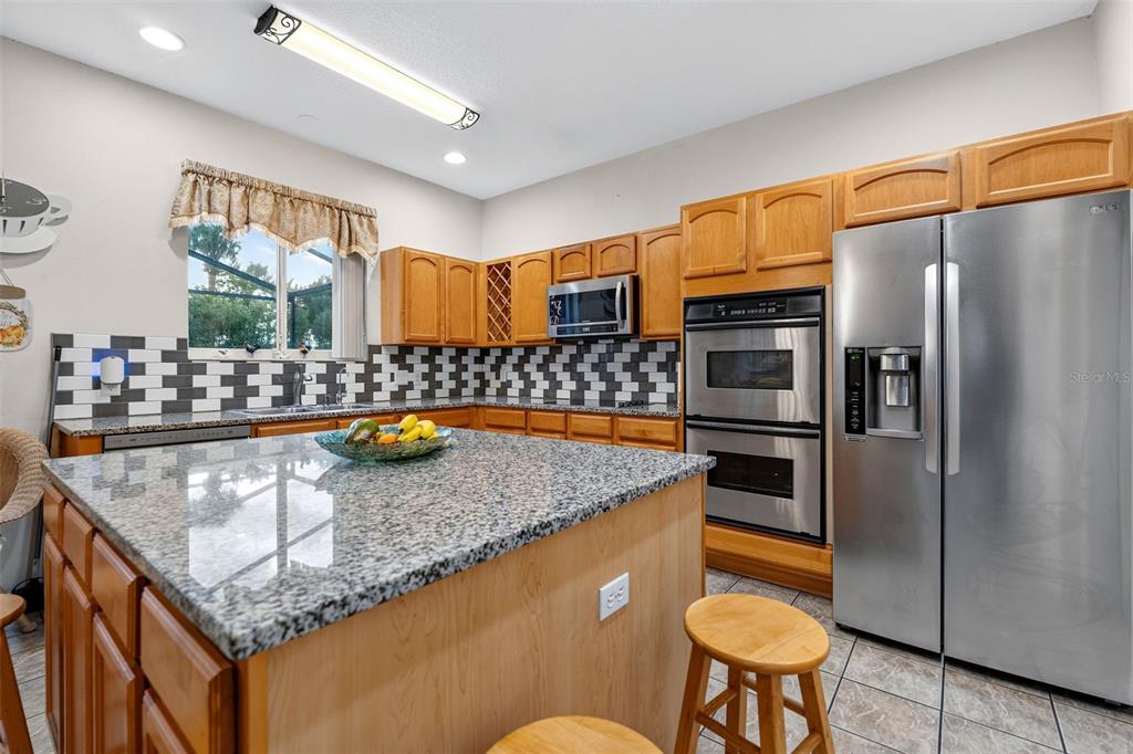 A kitchen features light wood cabinets, granite countertops, a central island, and stainless steel appliances — 16525 SUNRISE VISTA DRIVE, CLERMONT, FL