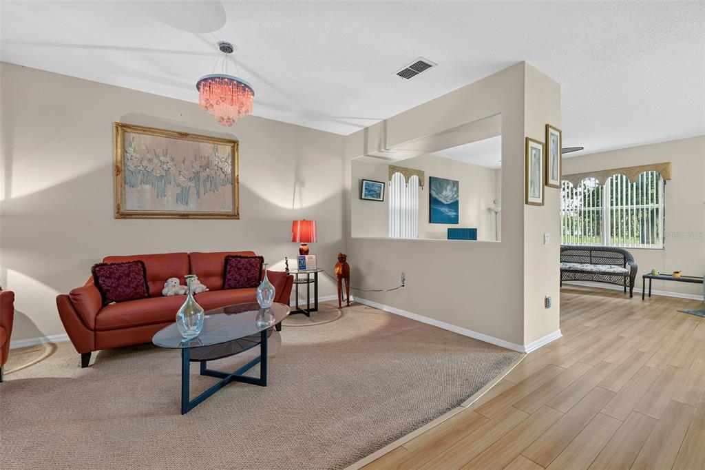 A living room features a red sofa, a glass coffee table, and beige carpeting — 16525 SUNRISE VISTA DRIVE, CLERMONT, FL