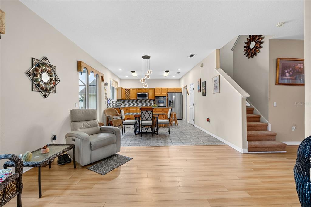 An open-concept living area features light wood flooring, a kitchen with wooden cabinets, and stairs — 16525 SUNRISE VISTA DRIVE, CLERMONT, FL