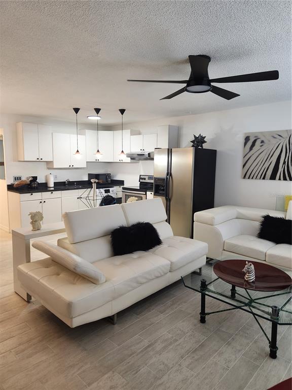 An open-concept living room and kitchen featuring white cabinetry, stainless appliances, and white leather sofas — 9101 W HILLSBOROUGH AVENUE UNIT I209, TAMPA, FL