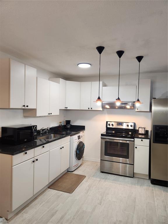 A kitchen features white cabinets, black countertops, stainless steel appliances, and a built-in washer — 9101 W HILLSBOROUGH AVENUE UNIT I209, TAMPA, FL
