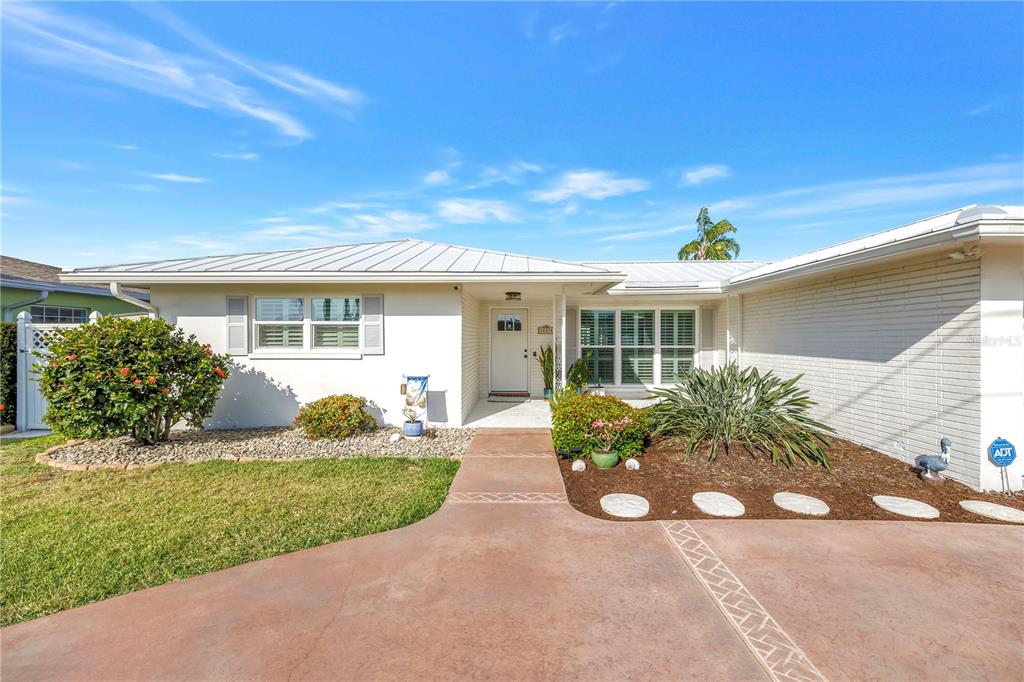 A single-story house with a white brick exterior, metal roof, and a concrete driveway — 12475 4TH STREET E, TREASURE ISLAND, FL