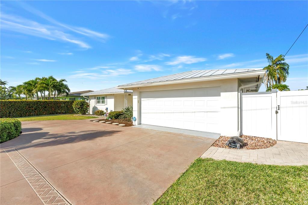 A white house with a two-car garage and a paved driveway under a blue sky — 12475 4TH STREET E, TREASURE ISLAND, FL