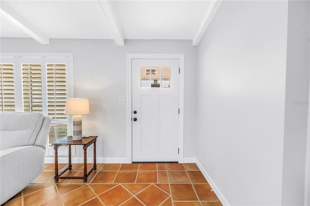 An entryway features a white door, terracotta tile flooring, and a side table with a lamp — 12475 4TH STREET E, TREASURE ISLAND, FL