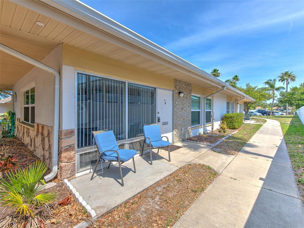 A concrete patio with two blue chairs sits in front of a single-story building — 4313 TAHITIAN GARDENS CIRCLE UNIT K, HOLIDAY, FL