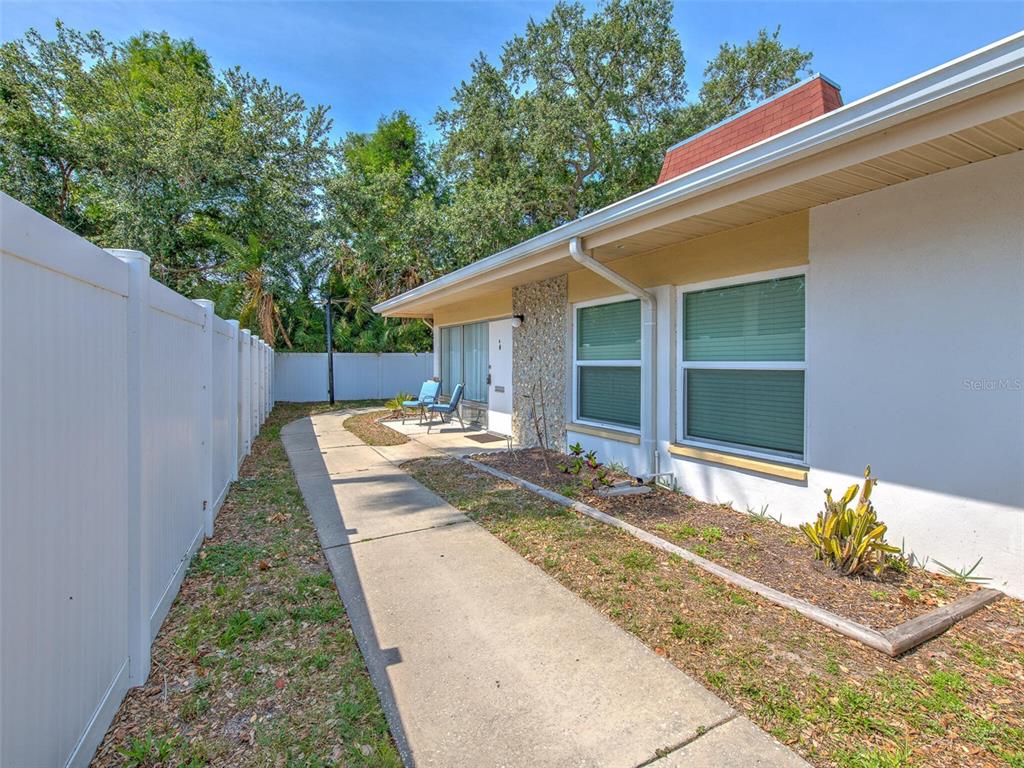 A concrete walkway leads along the side of a white house with a stone accent wall — 4313 TAHITIAN GARDENS CIRCLE UNIT K, HOLIDAY, FL