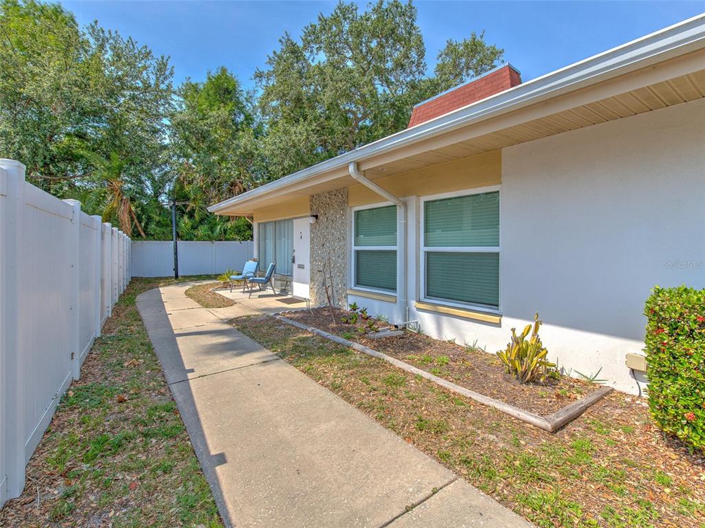 A concrete walkway leads to the entrance of a white house with a stone accent wall — 4313 TAHITIAN GARDENS CIRCLE UNIT K, HOLIDAY, FL
