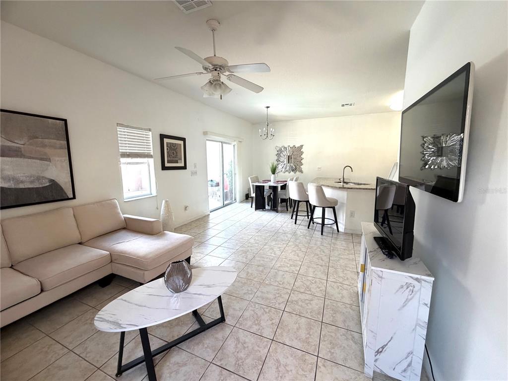 An open-concept living and dining area features tile flooring, a white sectional, and a kitchen island — 4573 ADA LANE, KISSIMMEE, FL