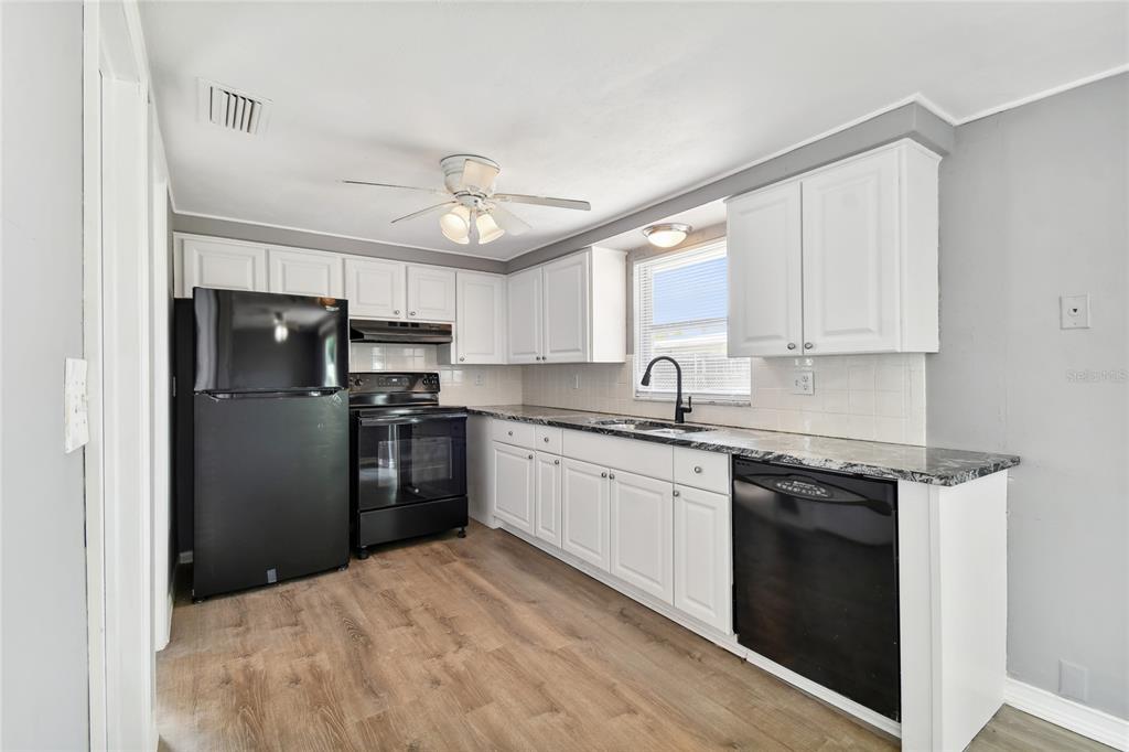 A kitchen features white cabinets, black appliances, granite countertops, and wood-look flooring — 7721 ARBORDALE DRIVE, PORT RICHEY, FL