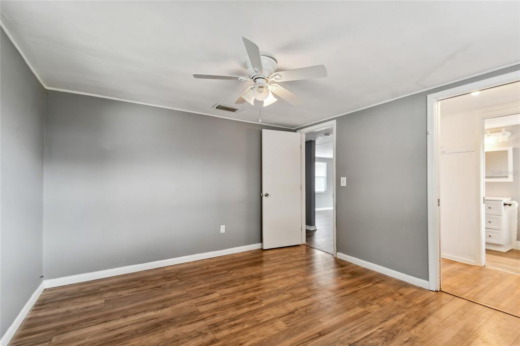 An empty bedroom features gray walls, wood-look flooring, a ceiling fan, and two doorways — 7721 ARBORDALE DRIVE, PORT RICHEY, FL