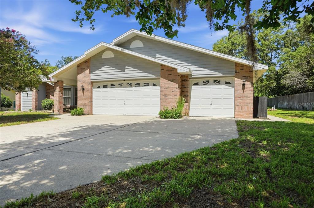 A single-story house with a brick facade, gray siding, and two white garage doors — 18451 WINDING OAKS BOULEVARD, HUDSON, FL