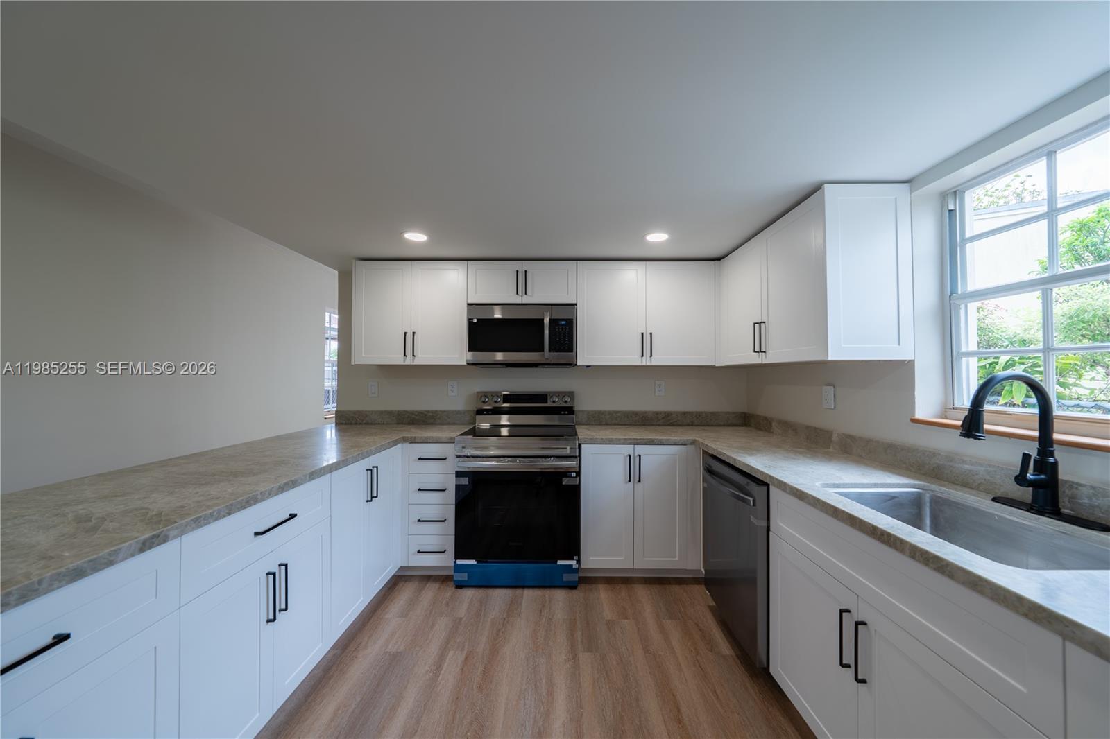 A kitchen features white cabinets, stainless steel appliances, stone-look countertops, and a window — 370 Flagami Blvd, Miami FL 33144, MIAMI, FL