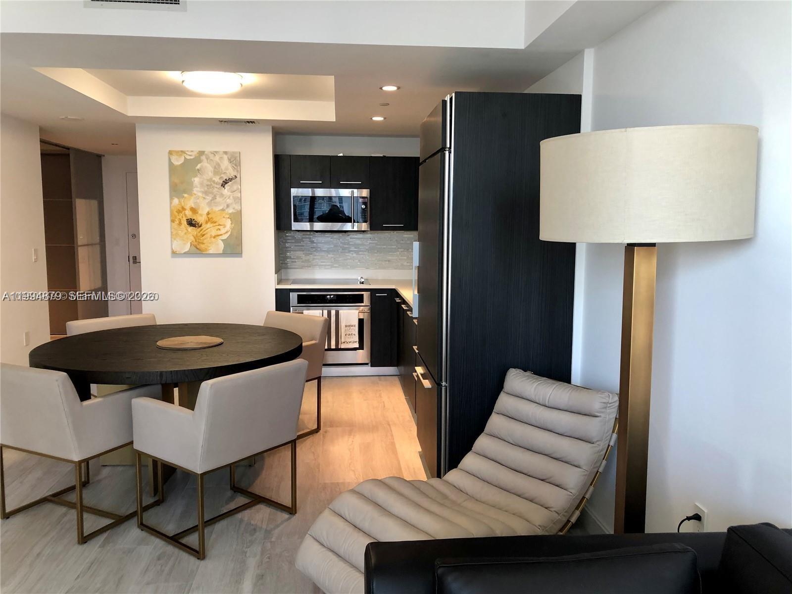 A modern kitchen with dark cabinetry and stainless steel appliances sits beside a dining area — 45 SW 9th St # 2004, Miami FL 33130, MIAMI, FL
