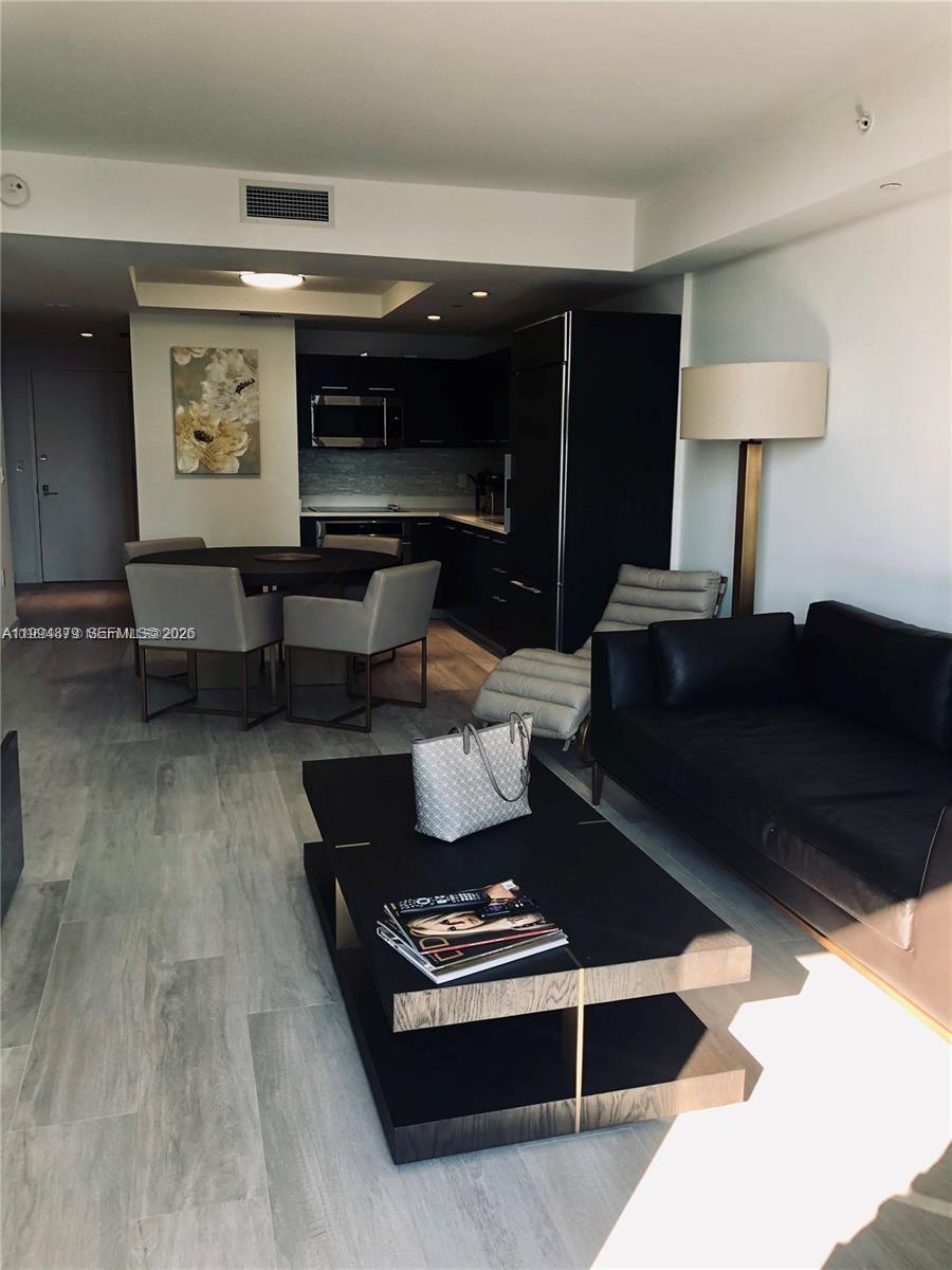 A modern living room and kitchen area feature dark cabinetry, a black sofa, and light flooring — 45 SW 9th St # 2004, Miami FL 33130, MIAMI, FL