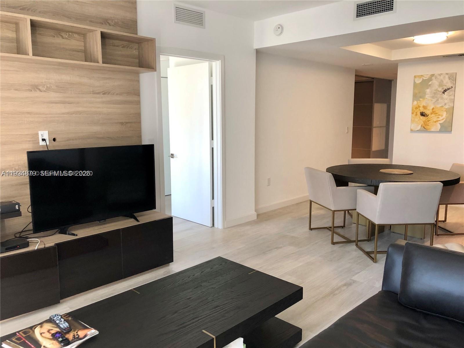 A living room features a television, wood-paneled wall, and a dining area with round table — 45 SW 9th St # 2004, Miami FL 33130, MIAMI, FL