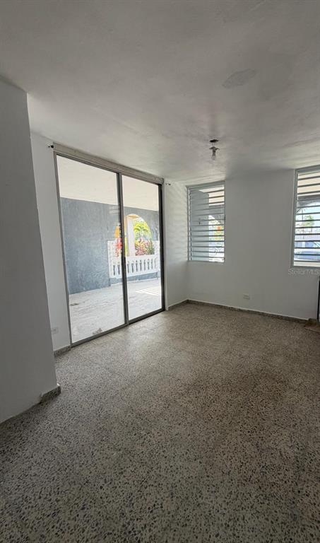 An empty room with terrazzo floors, white walls, sliding glass doors, and louvered windows — Villa Carolina 205-13 N 510, CAROLINA, PR