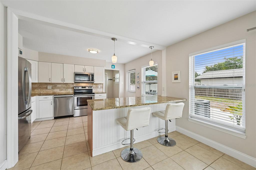 A kitchen features white cabinets, stainless steel appliances, a granite island, and two bar stools — 5005 BEE RIDGE ROAD, SARASOTA, FL