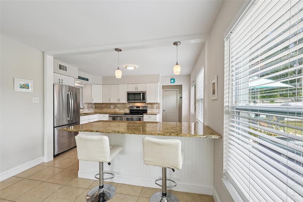 A kitchen features white cabinetry, granite countertops, stainless steel appliances, and two bar stools — 5005 BEE RIDGE ROAD, SARASOTA, FL