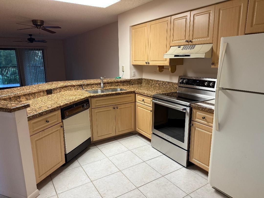 A kitchen features light wood cabinets, granite countertops, stainless steel appliances, and tile flooring — 2205 S Cypress Bend Drive # 307, Pompano Beach FL 33069, POMPANO BEACH, FL