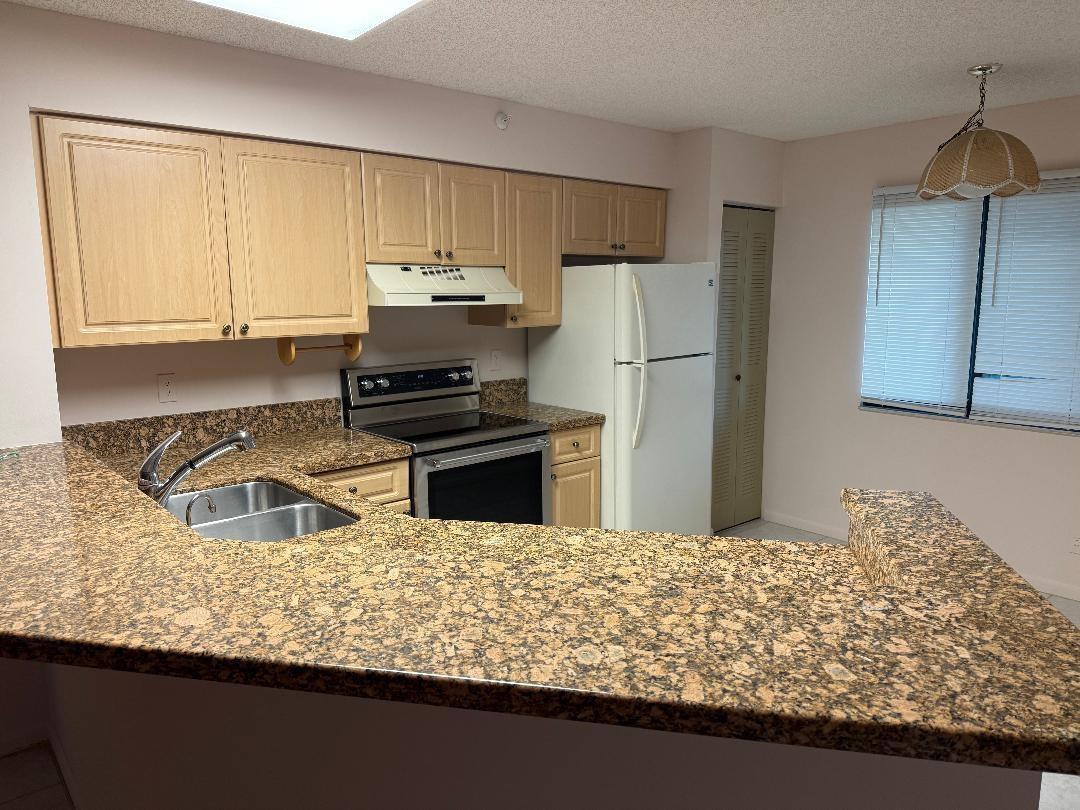 A kitchen features light wood cabinets, granite countertops, and white appliances — 2205 S Cypress Bend Drive # 307, Pompano Beach FL 33069, POMPANO BEACH, FL