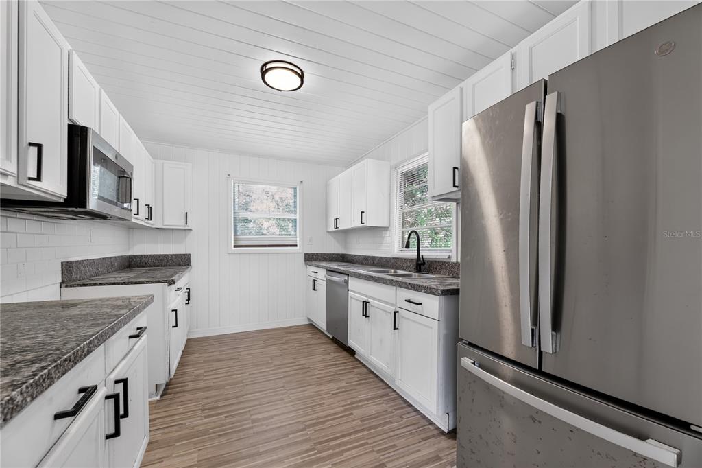 A kitchen features white cabinets, dark granite countertops, stainless steel appliances, and wood-look flooring — 3636 TURTON AVENUE, JACKSONVILLE, FL