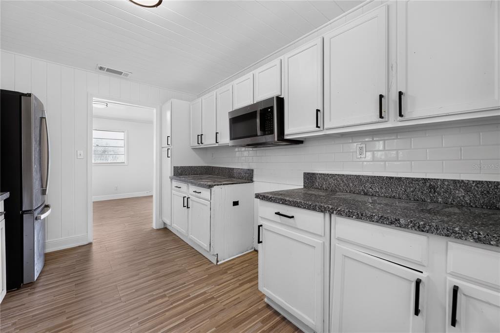A kitchen features white cabinets, dark granite countertops, a microwave, and light wood-look flooring — 3636 TURTON AVENUE, JACKSONVILLE, FL