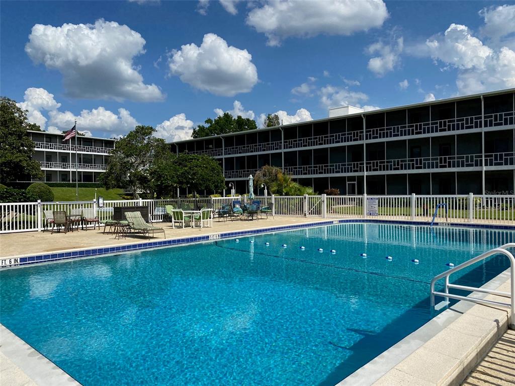A swimming pool sits in front of a multi-story apartment building with screened balconies — 1700 6TH STREET NW UNIT C1, WINTER HAVEN, FL